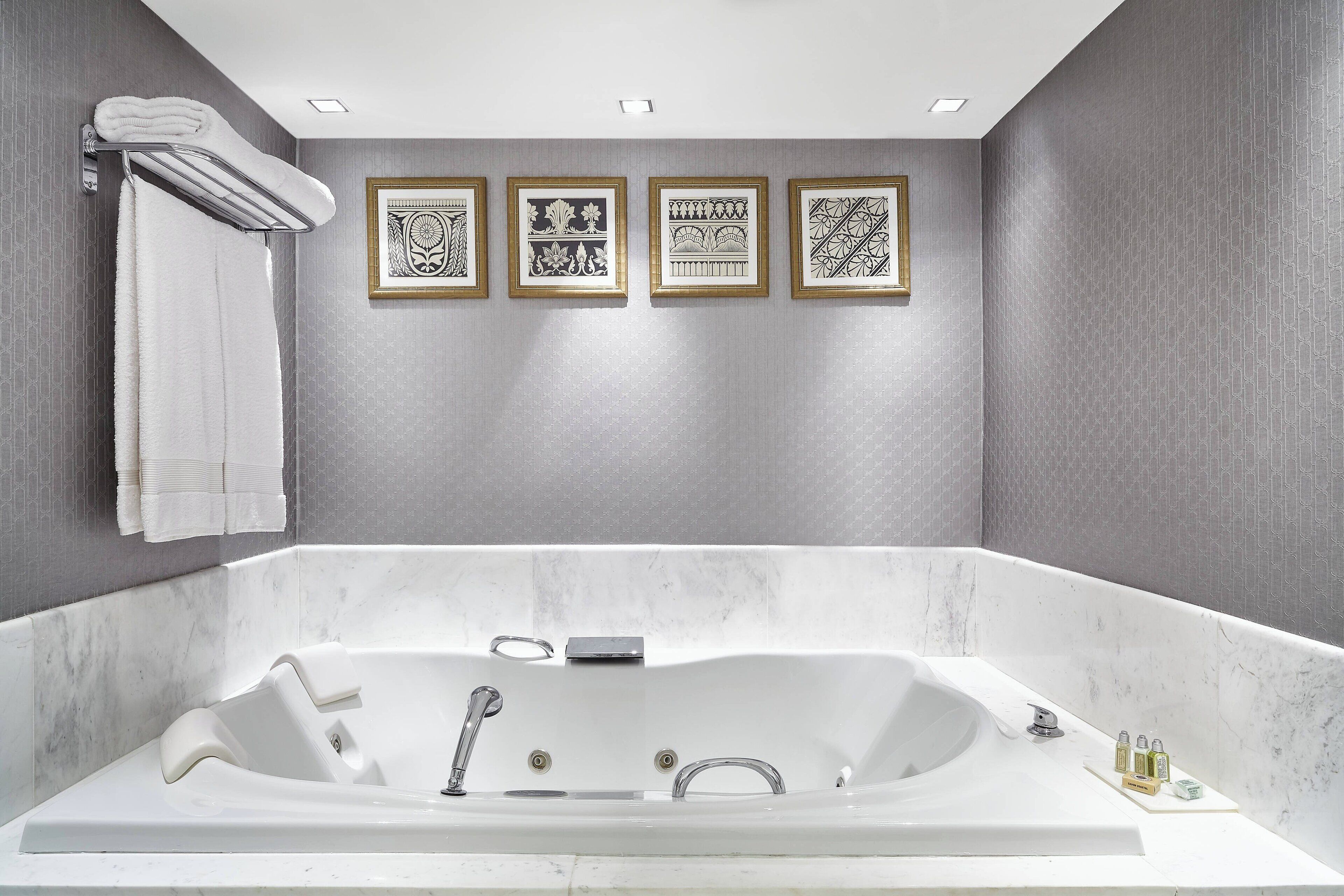 A modern bathroom with a large bathtub, a towel rack, and four framed wall art pieces.