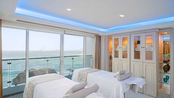 A room with two beds, a massage table, and a view of the sea.