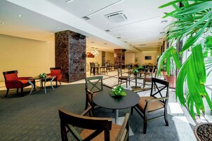 A hotel lobby with multiple seating areas, including round tables and chairs, and a large indoor plant.