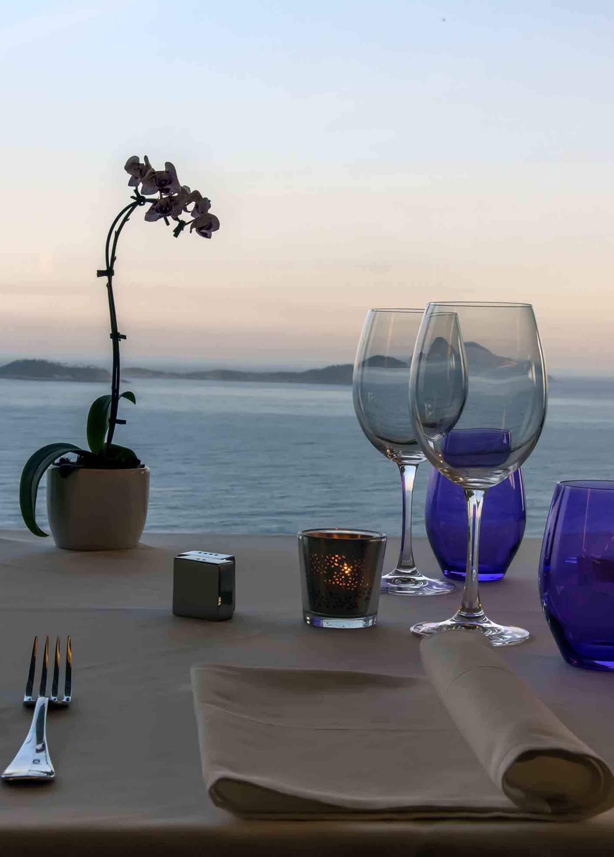 A table set for two with wine glasses, a candle, and a potted orchid.