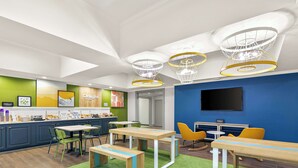 A modern hotel lobby with a dining area, green walls, and a TV screen. - Spark by Hilton Commerce, GA (Commerce)