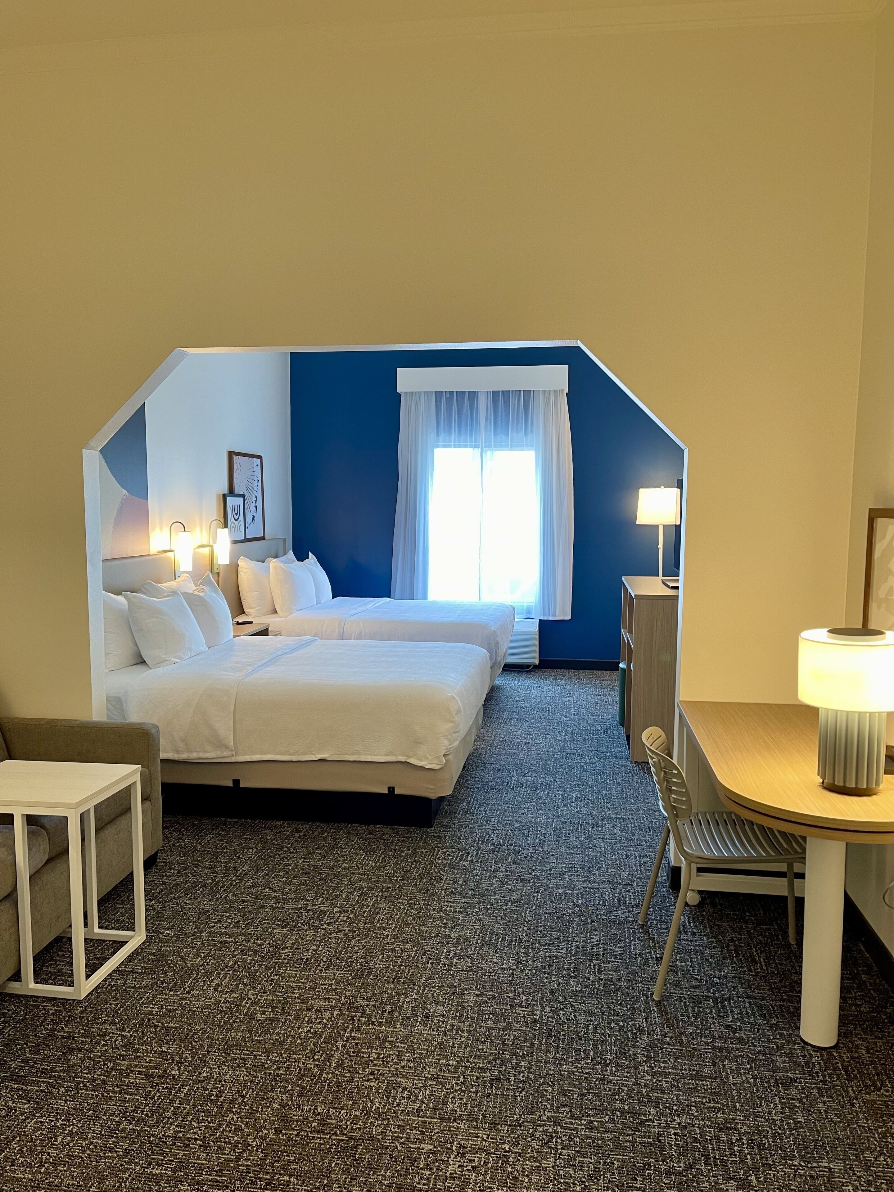 Habitación de hotel con cama, escritorio, silla y lámpara.