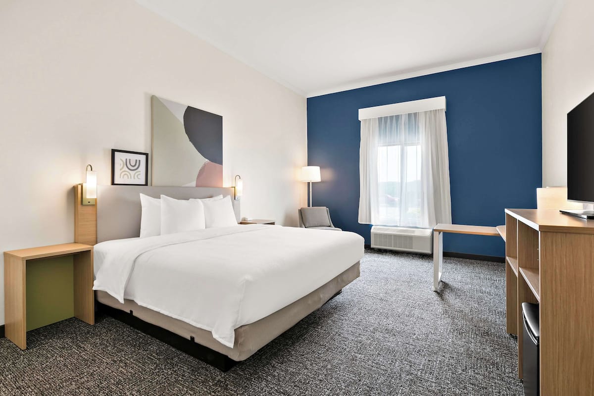 A hotel room with a large bed, bedside tables, a desk, and a window with curtains.