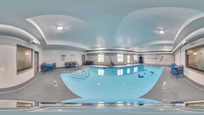 A large indoor swimming pool with a curved ceiling, surrounded by blue chairs and tables, and a clear view of the pool area. - Spark by Hilton Commerce, GA (Commerce)