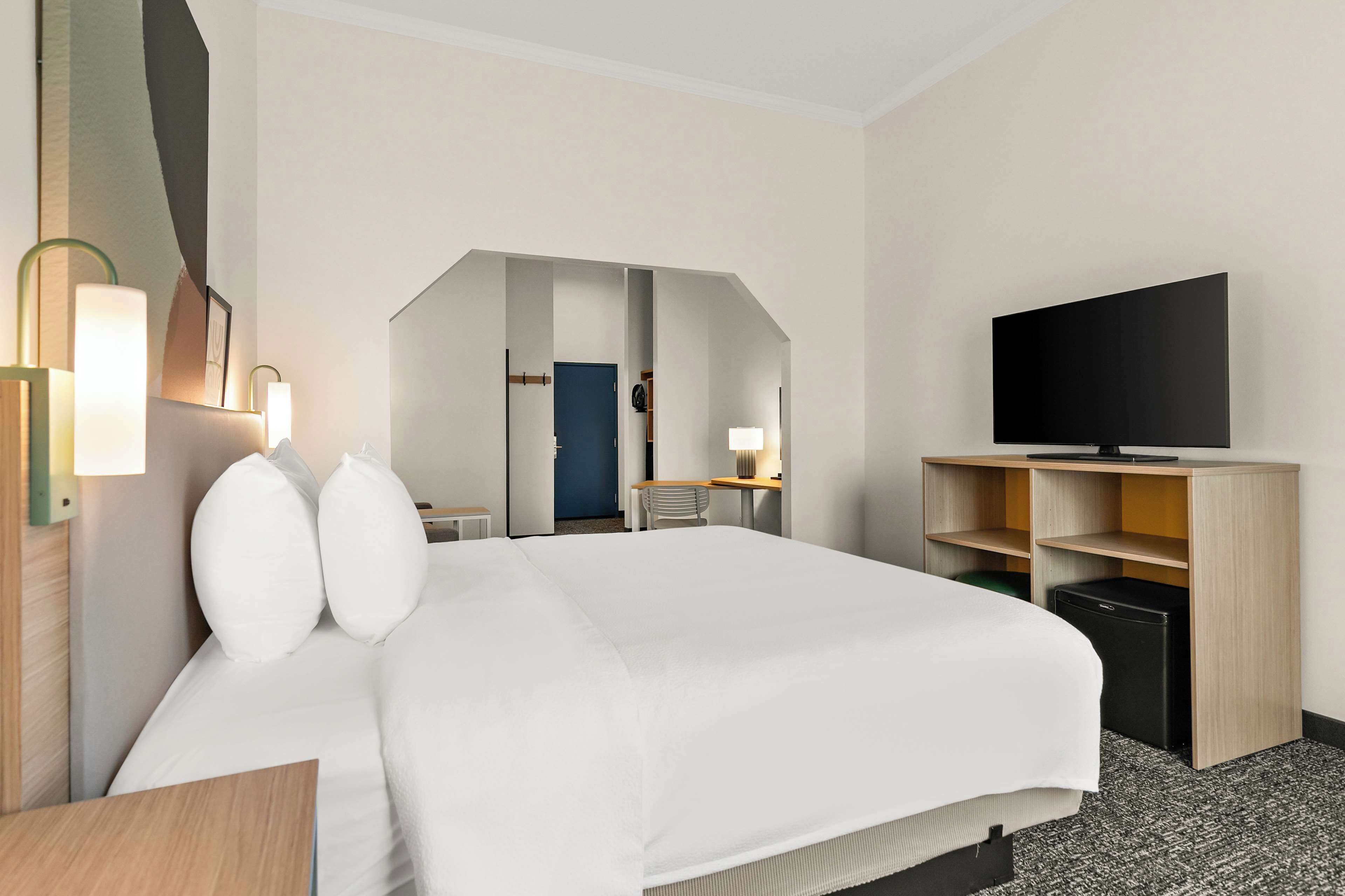 Habitación de hotel con una cama grande, lámparas de noche, un televisor de pantalla plana, un escritorio con silla y un armario.