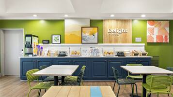 A hotel kitchen with a buffet setup, green chairs, and a 'Delight in the day' sign.