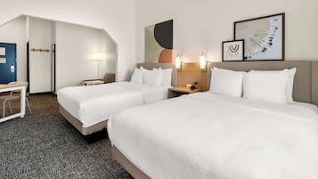 Habitación de hotel con dos camas, un escritorio y una silla. Hay lámparas de pared y una obra de arte enmarcada sobre las camas.