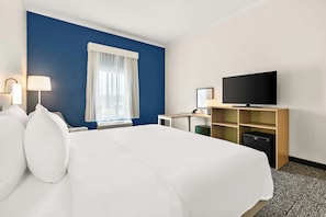 A hotel room with a large bed, a desk with a computer, a television, and a window with curtains.