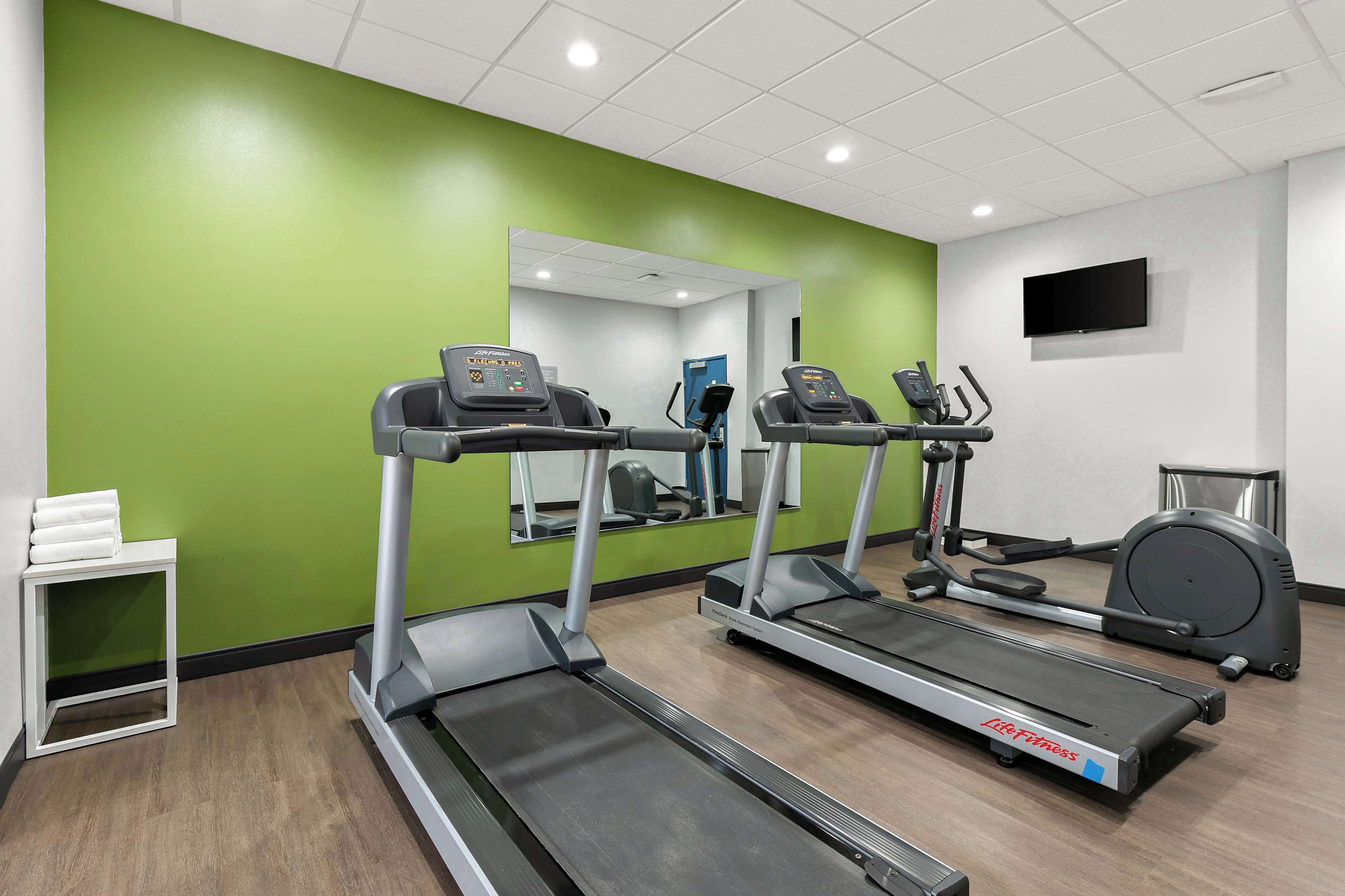 A fitness room with treadmills, a mirrored wall, and a television.