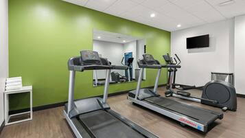 A fitness room with treadmills, a mirrored wall, and a television.