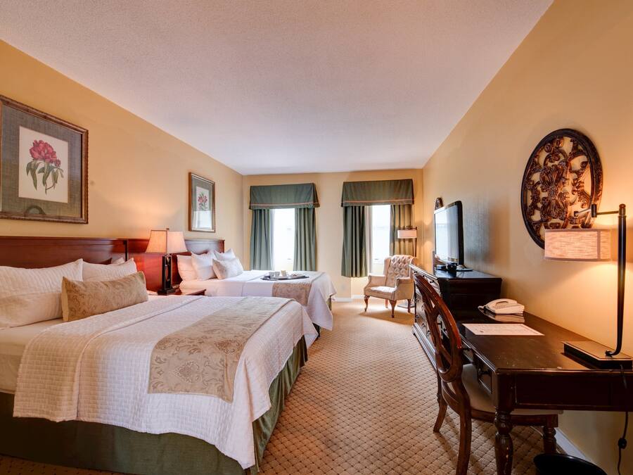 Quarto de hotel com duas camas, uma escrivaninha, uma cadeira, uma televisão e uma luminária de mesa.