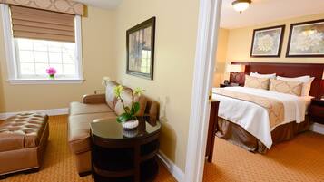 A hotel room with a bed, a sofa, a round table with a vase, and a window with blinds.