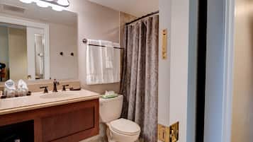 A bathroom with a vanity, sink, and toilet. There are towels hanging on a rack, and a shower curtain is visible.