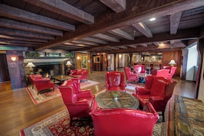 A spacious room with wooden beams, red leather chairs, a fireplace, and a bar area.