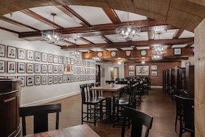 A dining area with wooden tables and chairs, framed pictures on the walls, and a brick wall.