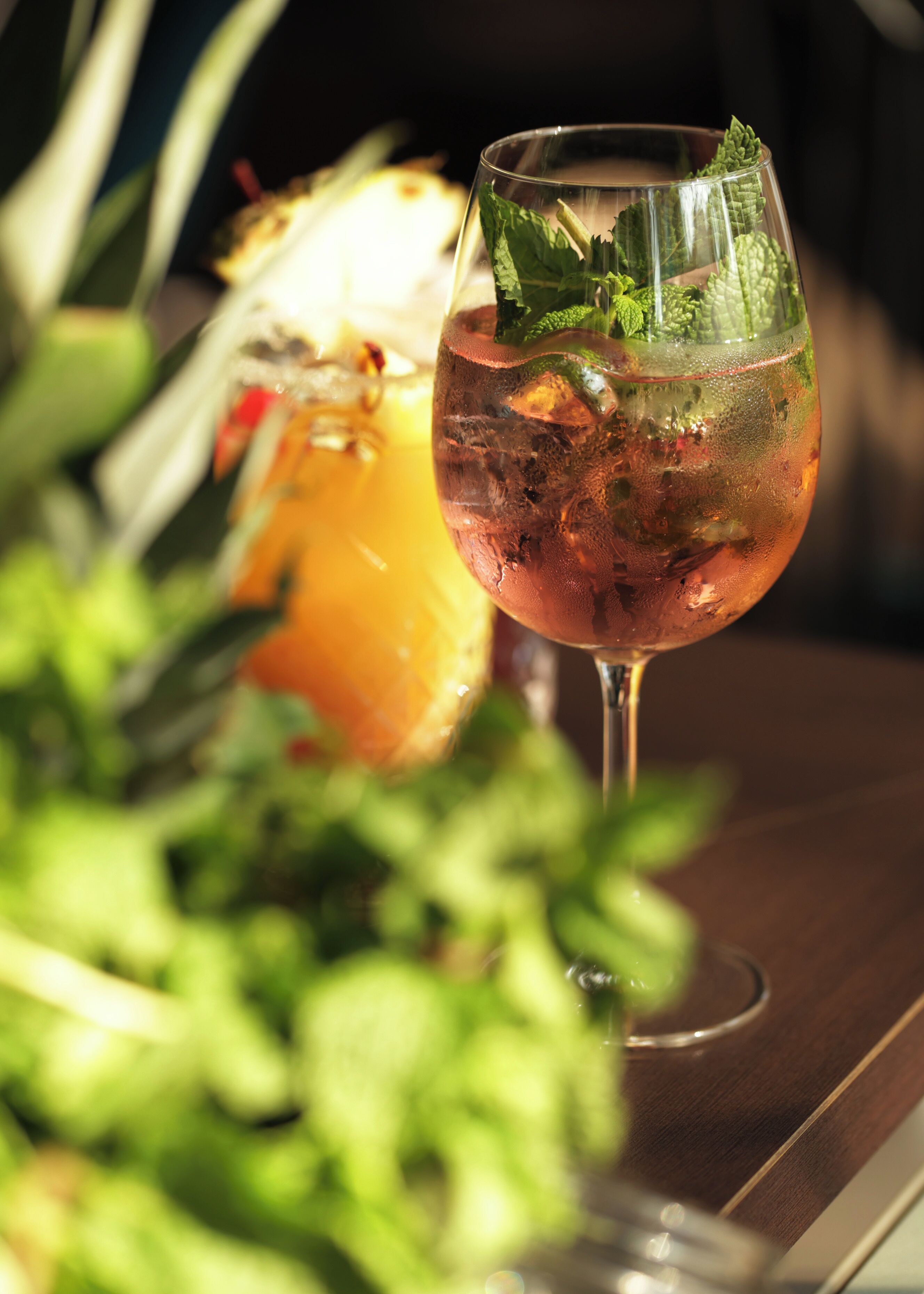 Ein Glas rosa Cocktail mit Minzblättern auf einem Holztisch.