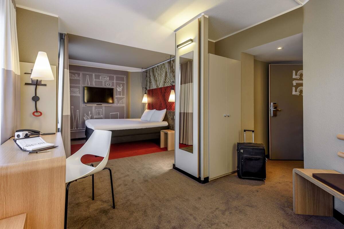Een hotelkamer met een bed, bureau, stoel, televisie en een kledingkast.
