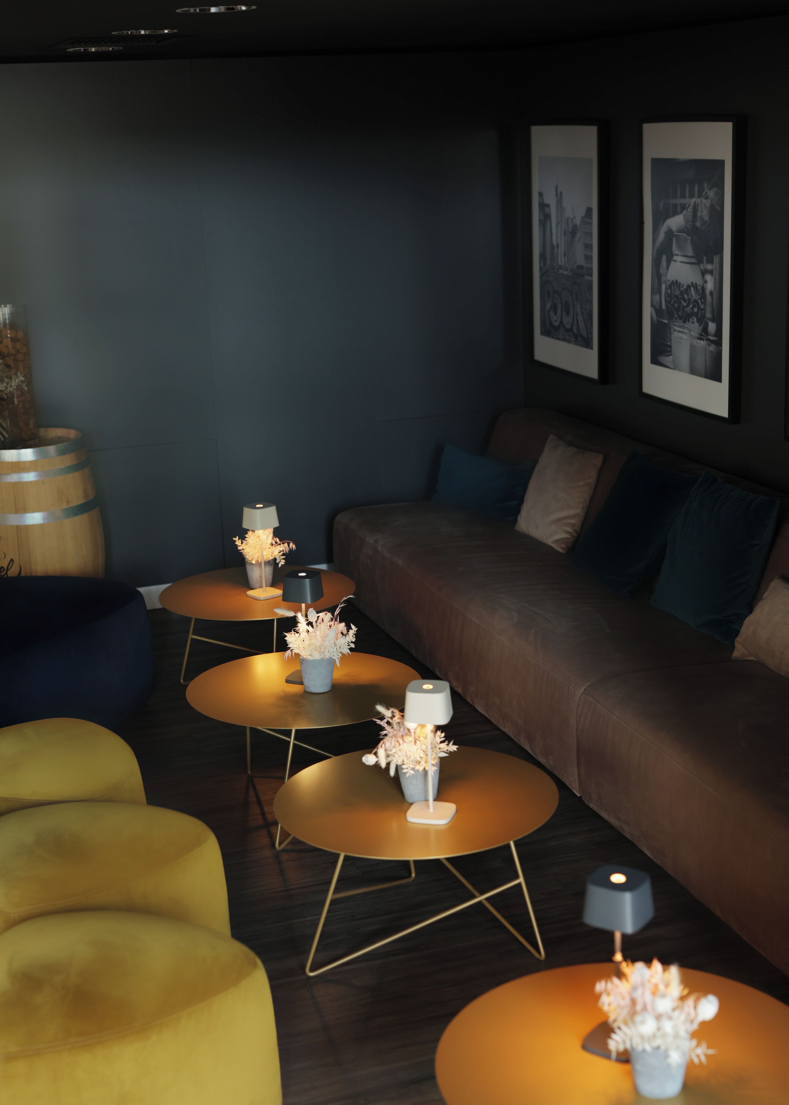 A modern lounge area with a sofa, round tables with lamps, and a decorative barrel.