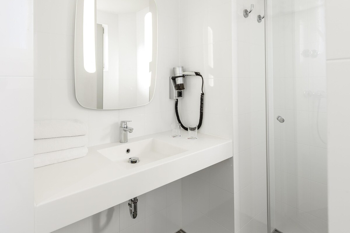 Un baño moderno con un lavamanos blanco, un espejo y un secador de pelo.