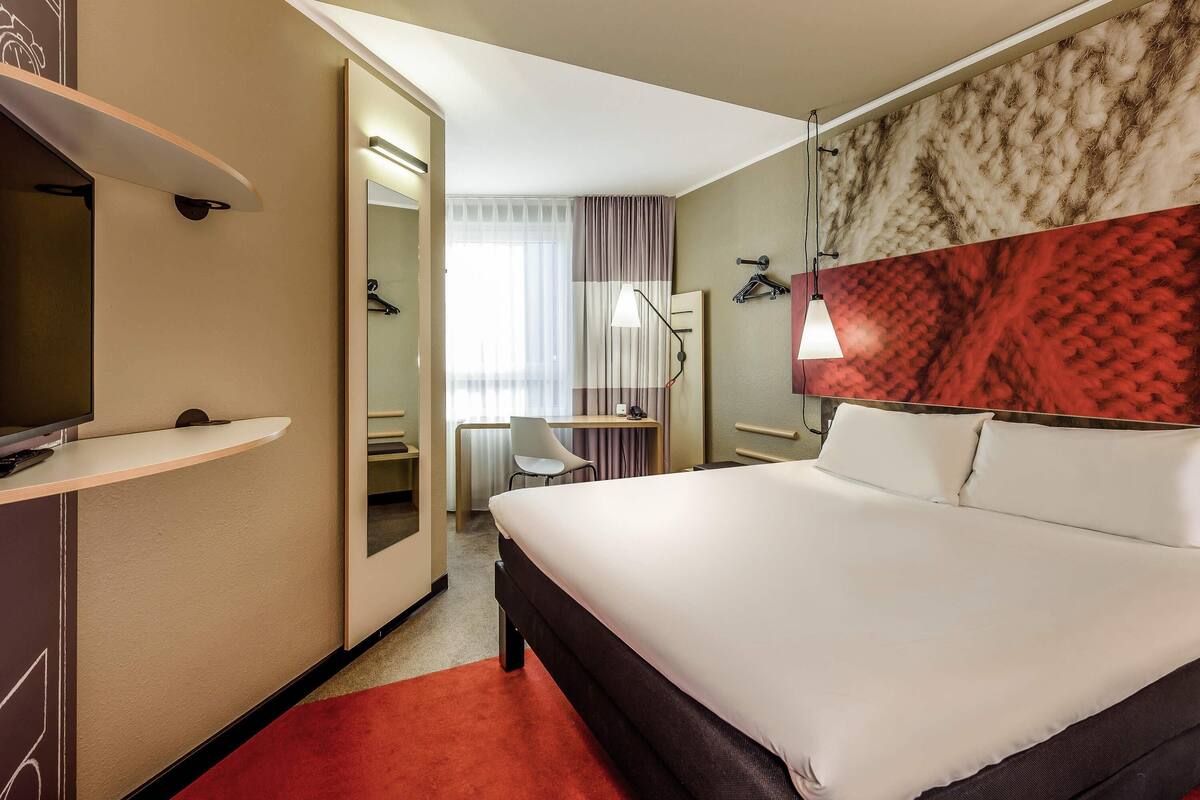 Een hotelkamer met een bed, een bureau, een stoel, een televisie en een kledingkast.