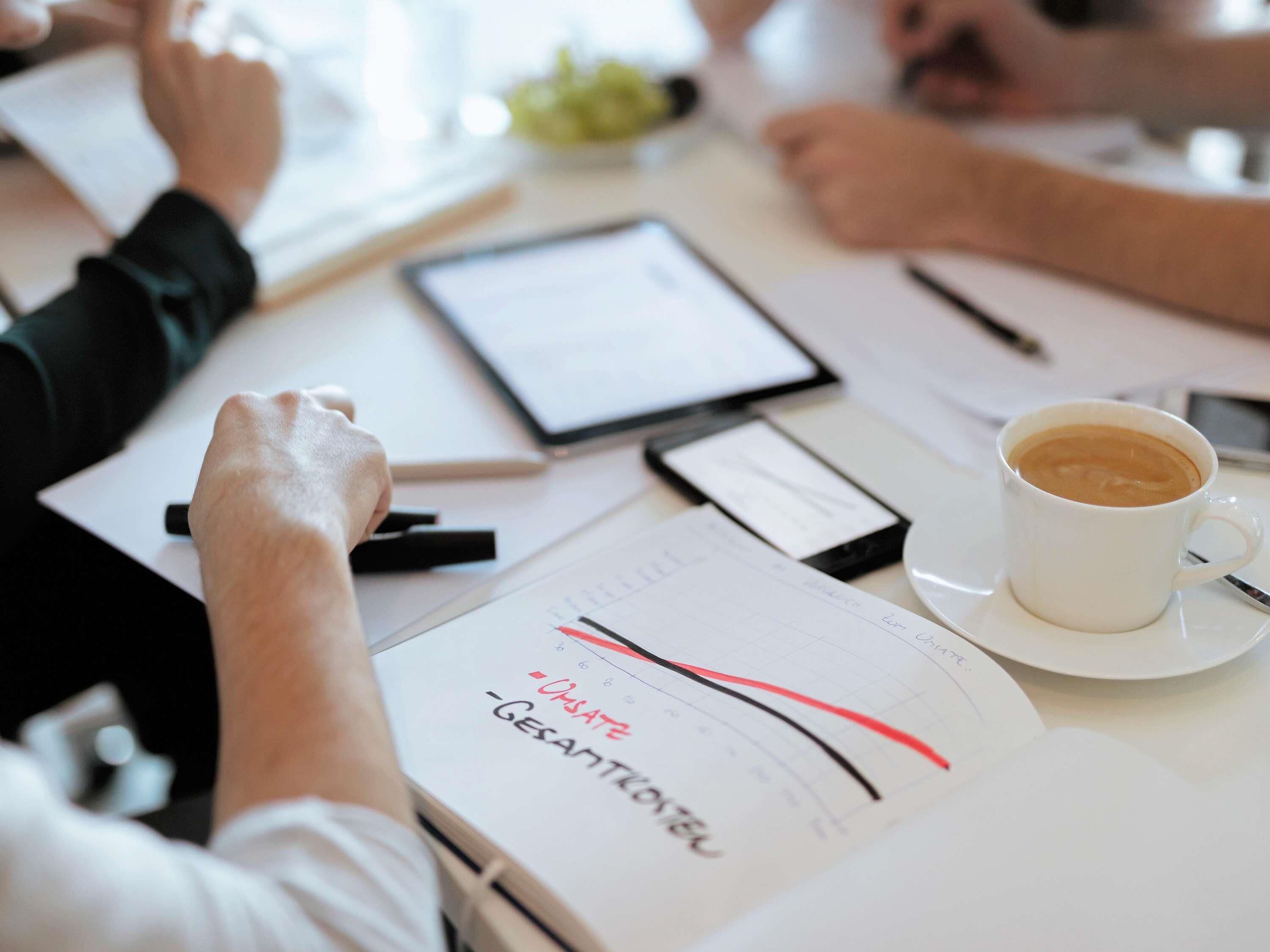 Papieren, een tablet en een koffiekop op een tafel.