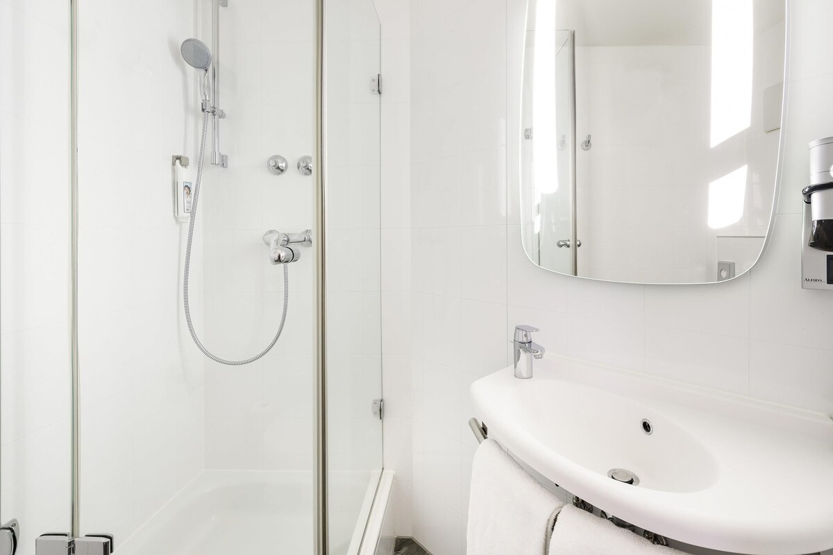 Un baño moderno con ducha de vidrio, lavamanos blanco y espejo grande.