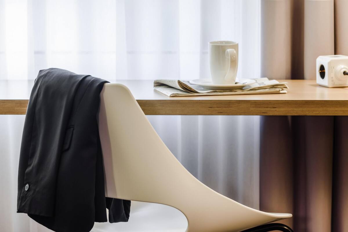 Een moderne hotelkamer met een houten bureau, een witte stoel, een kop en een printer.