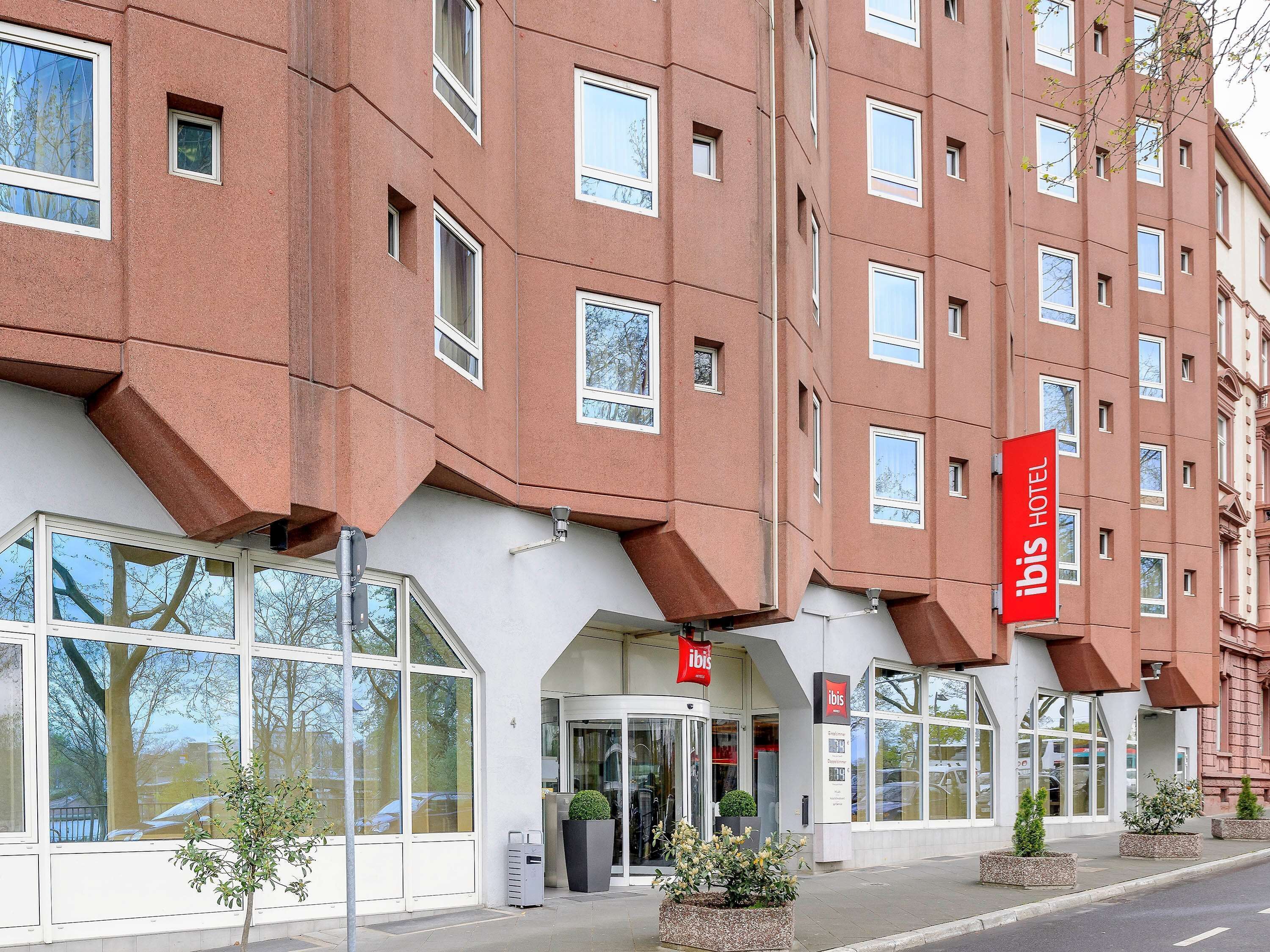 Un hôtel à la façade moderne, doté de grandes fenêtres et d’une enseigne rouge bien visible, indiquant qu’il s’agit d’un hôtel ibis.