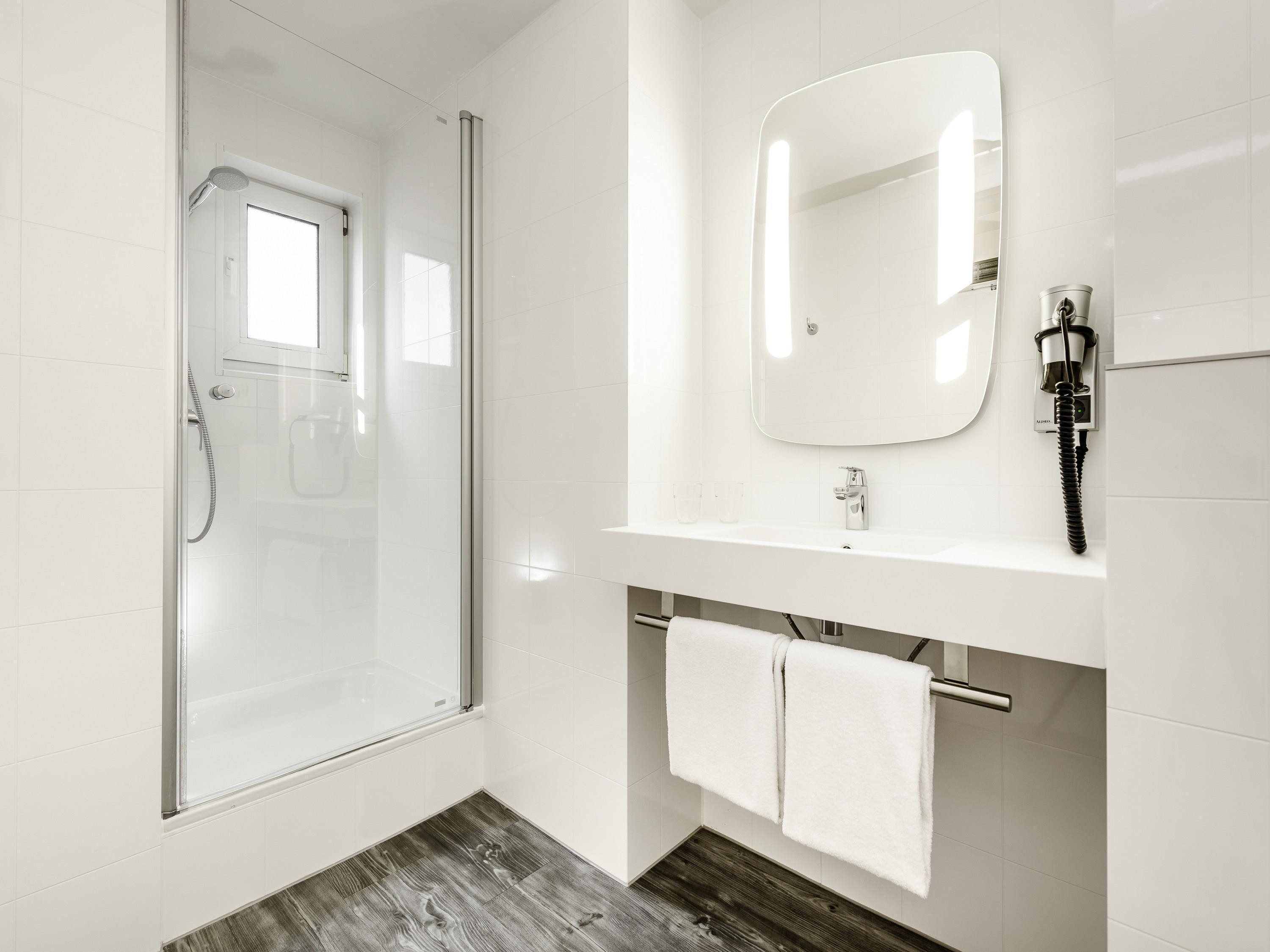 Een moderne badkamer met een douchecabine van glas, een witte wastafel met spiegel en een handdoekrek.