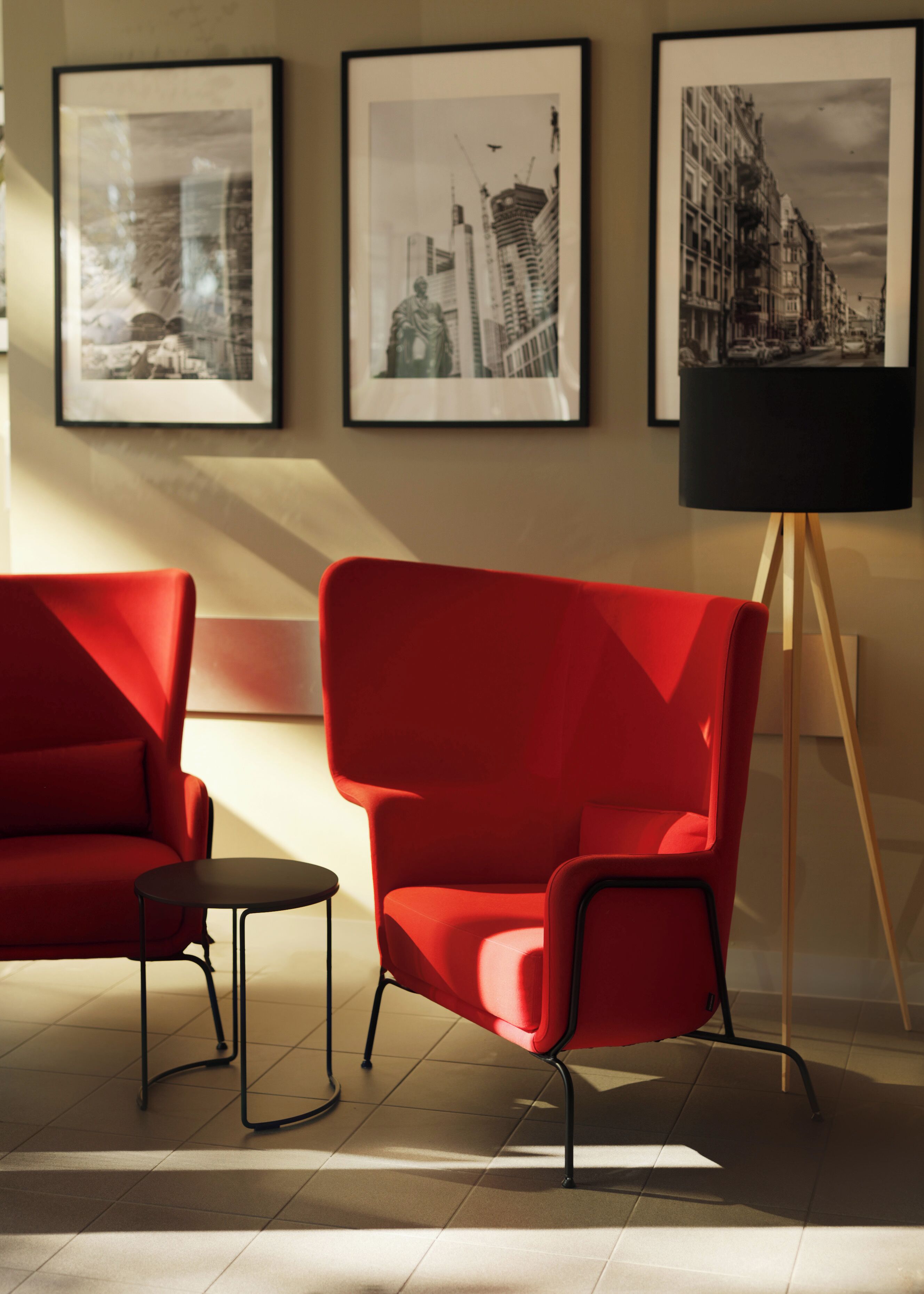 Una habitación moderna con un sillón rojo, una mesita auxiliar y una lámpara de pie. Hay tres cuadros enmarcados en la pared.