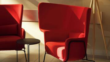 Una habitación moderna con un sillón rojo, una mesita auxiliar y una lámpara de pie. Hay tres cuadros enmarcados en la pared.