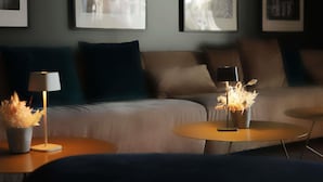 Une chambre d’hôtel moderne, équipée d’un canapé, de deux tables d’appoint, d’une lampe et de plantes décoratives.