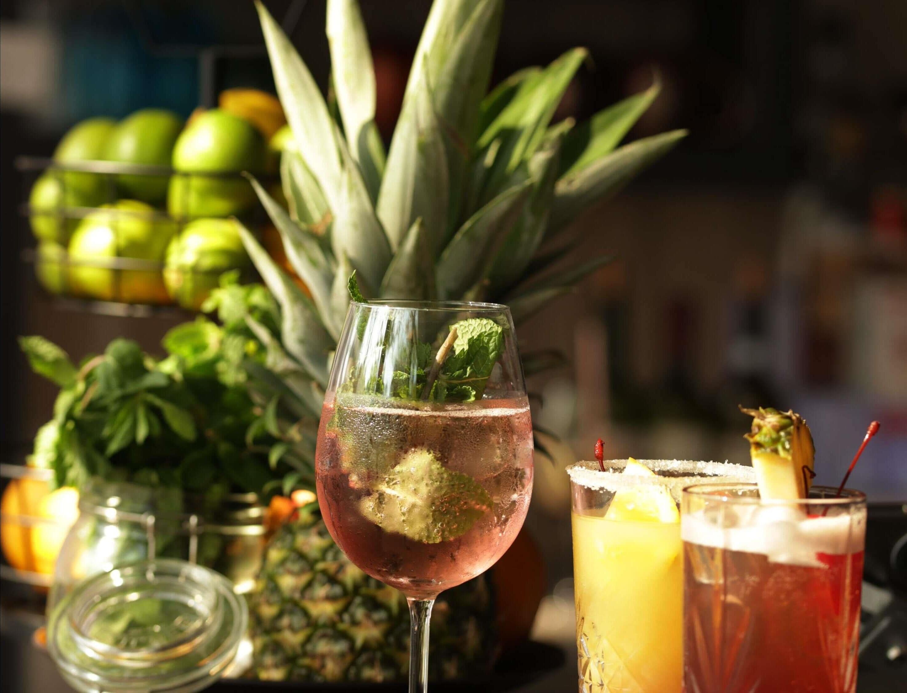 Un verre de boisson à la menthe et aux glaçons, un ananas et un verre de jus d’orange avec une paille.