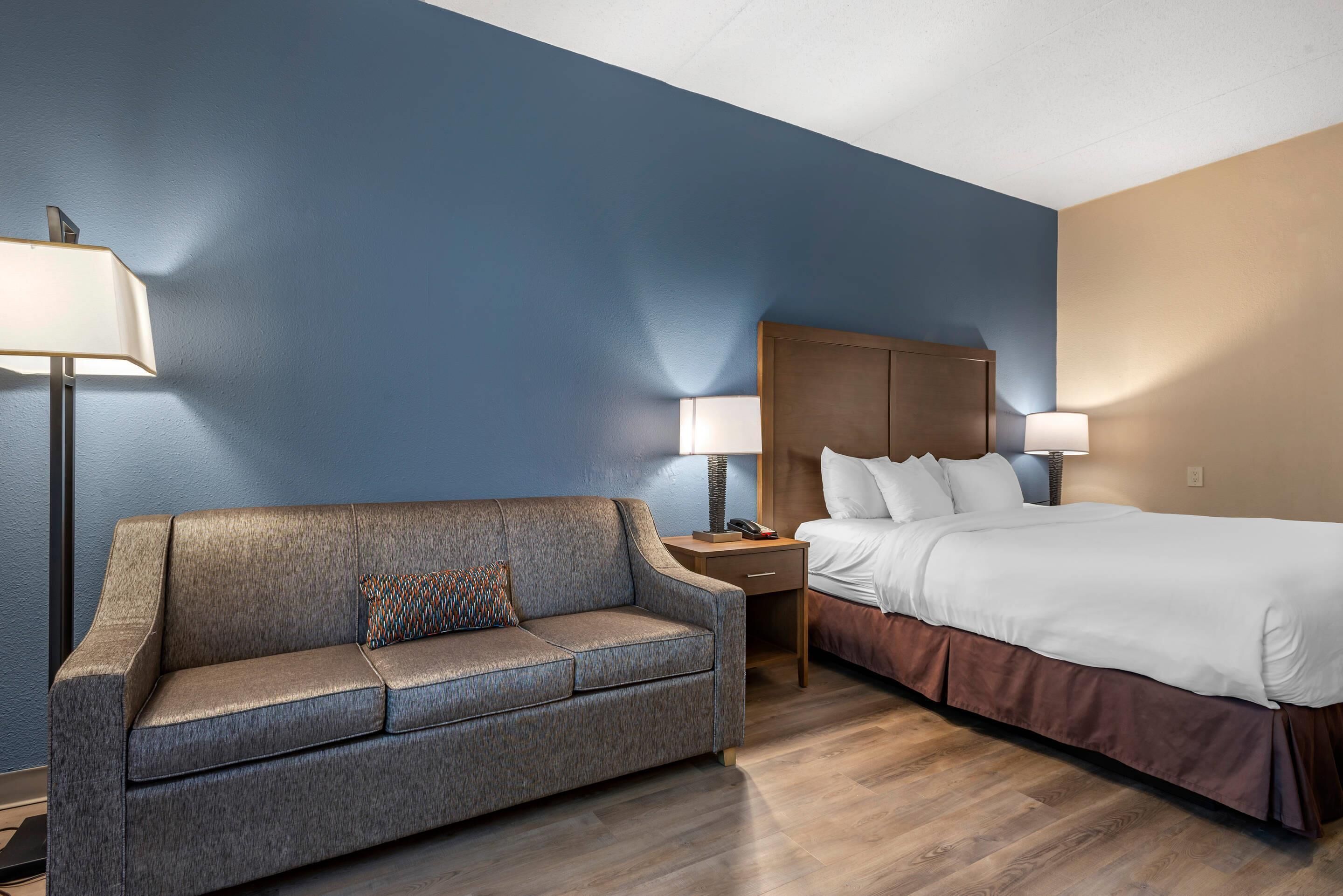 A hotel room with a sofa, a bed, a nightstand, and two lamps.