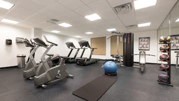 A gym with treadmills, elliptical machines, a stationary bike, a blue exercise ball, and a rack of sports balls.