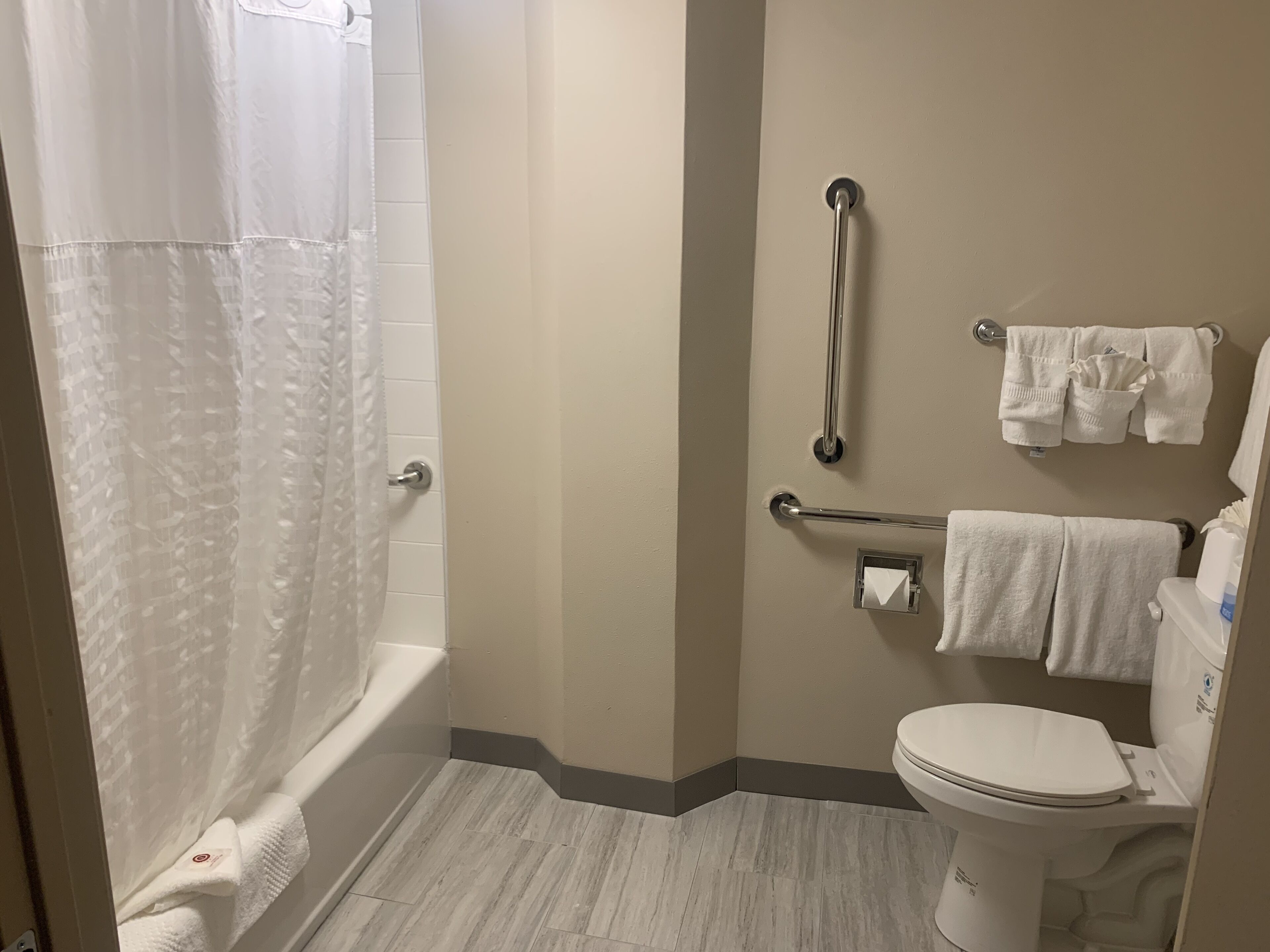 A bathroom with a bathtub, toilet, and handrails.