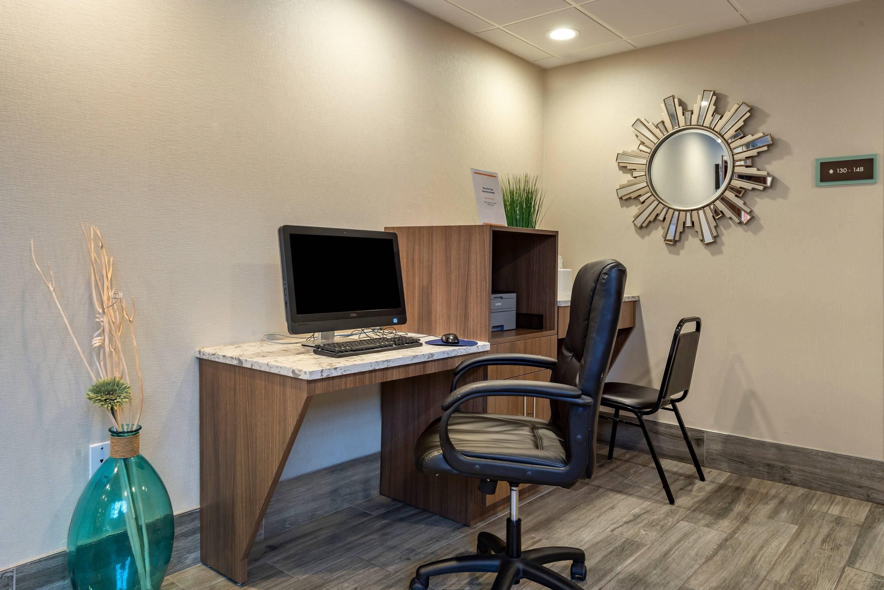 A modern office desk with a computer, two chairs, a decorative mirror, and a plant.