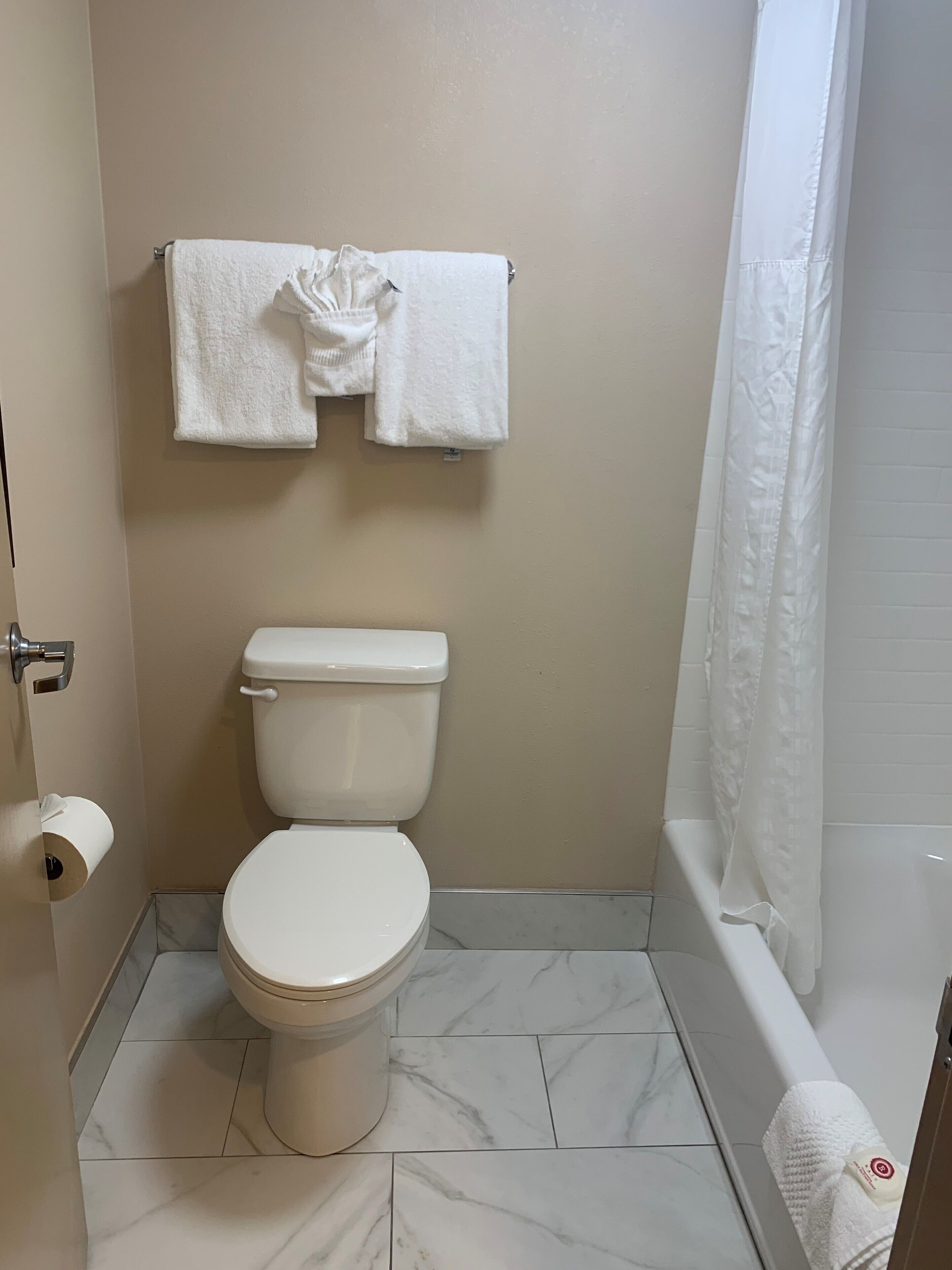 A bathroom with a toilet, a towel rack with two towels, a shower curtain, and a toilet paper holder.
