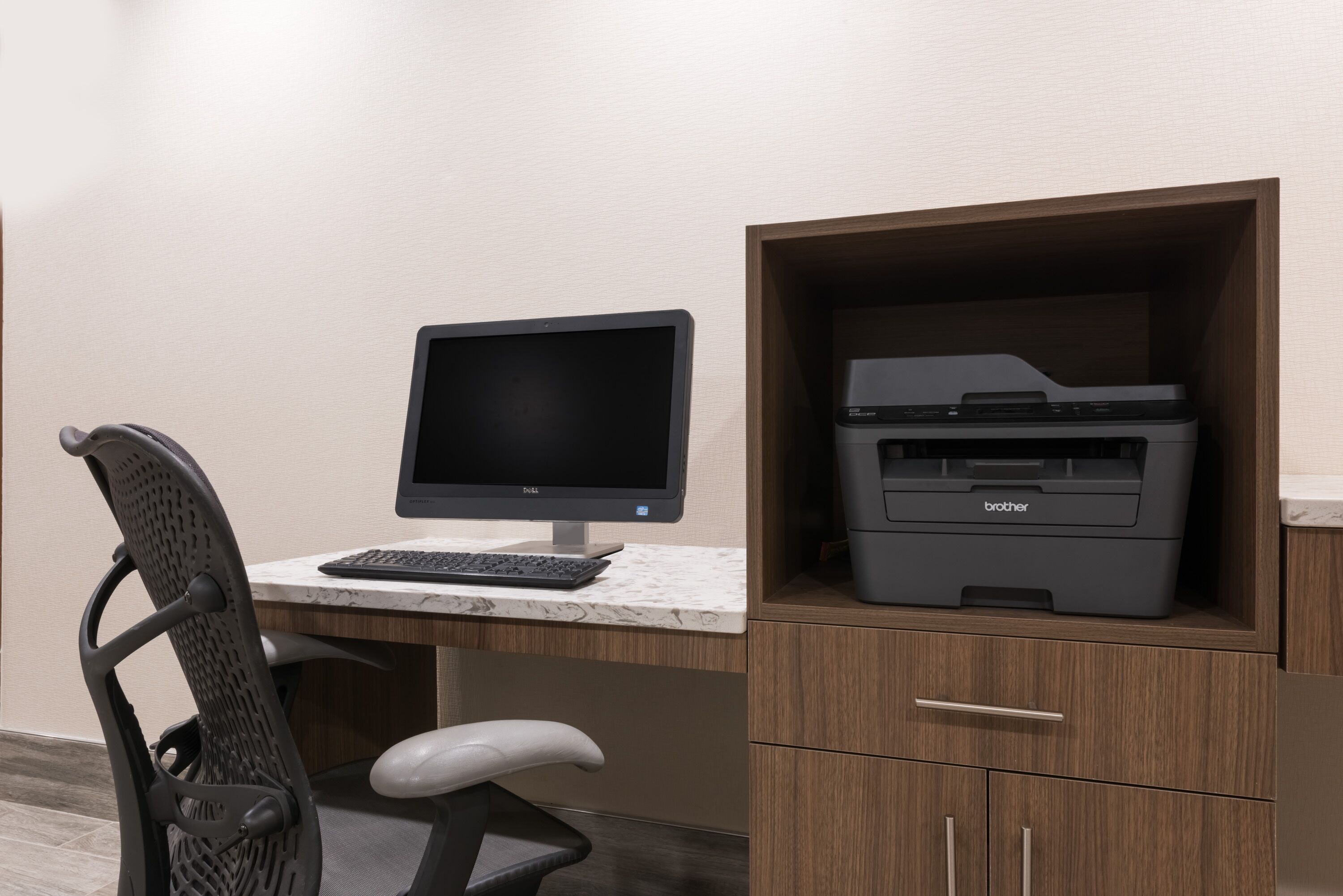 Un espacio de trabajo con un monitor Dell, una impresora Brother y una silla de oficina blanca.