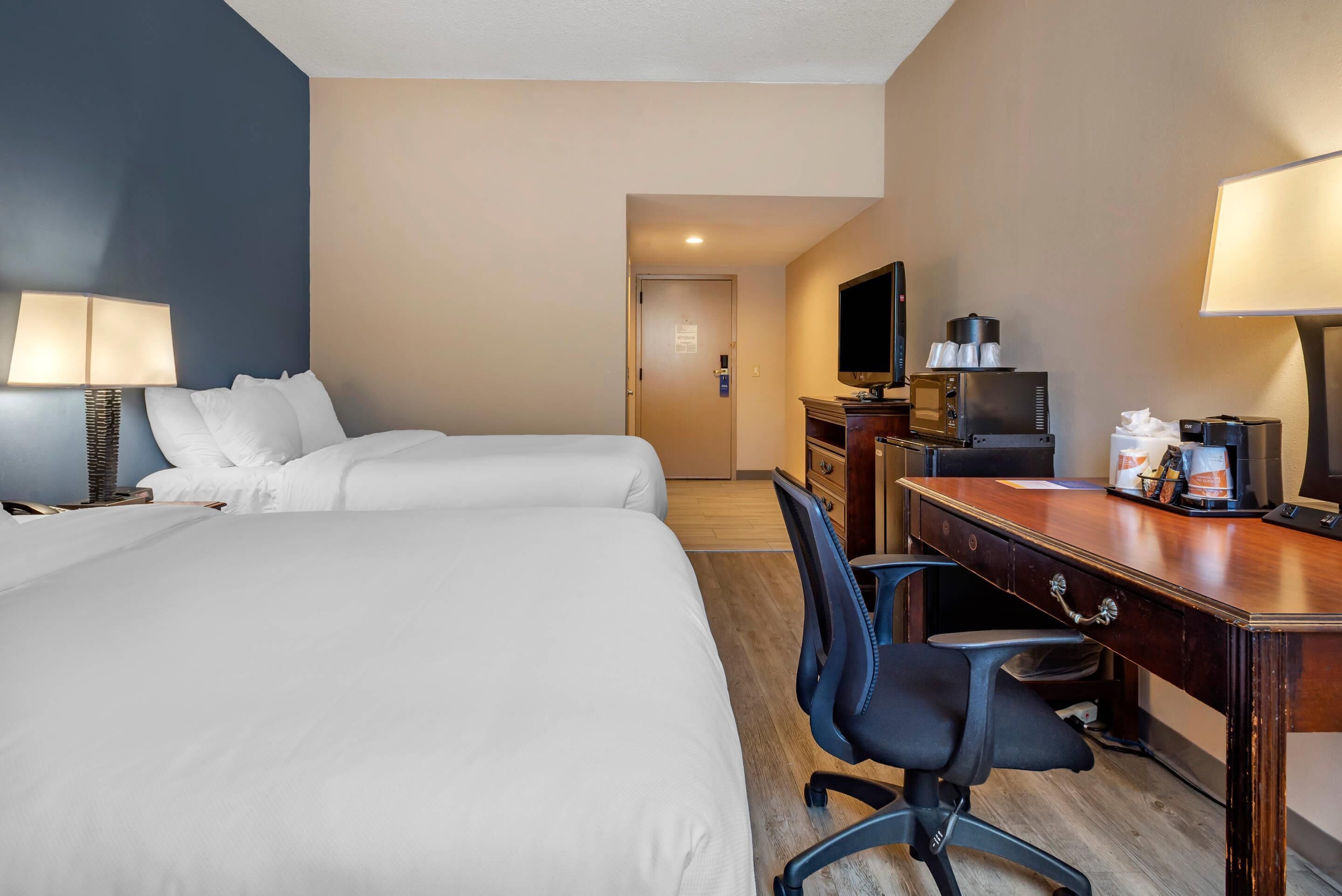 A hotel room with two beds, a desk with a computer, a TV, and a coffee machine.