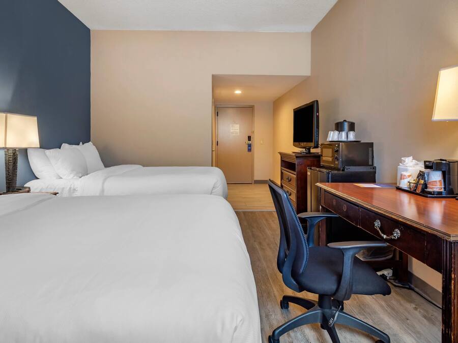A hotel room with two beds, a desk with a computer, a TV, and a coffee machine.