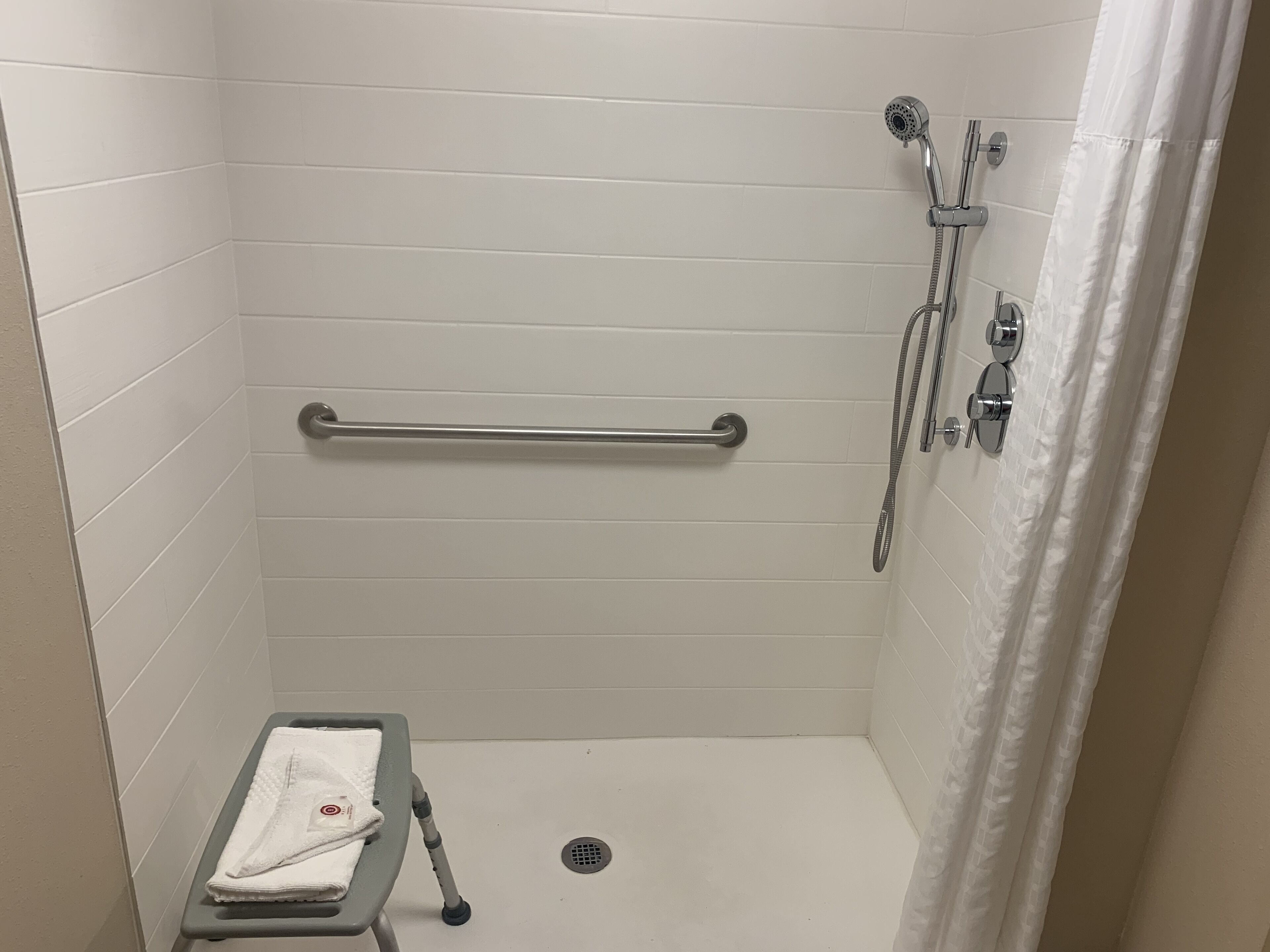 Une petite cabine de douche aux murs recouverts de carreaux blancs, équipée d’une barre d’appui, d’un pommeau de douche et d’un flexible de douche.