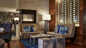 A modern living room with a fireplace, two sofas with patterned cushions, a coffee table, and a wall of wine bottles. - Renaissance Asheville Downtown Hotel (Asheville)