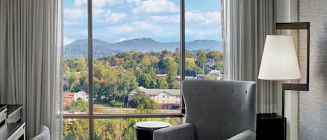 A hotel room with a large window offering a view of a mountainous landscape and residential buildings.