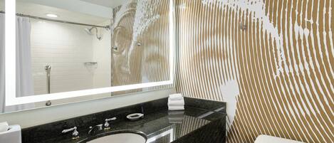 Un baño con lavamanos de granito negro, inodoro blanco y espejo con marco iluminado.