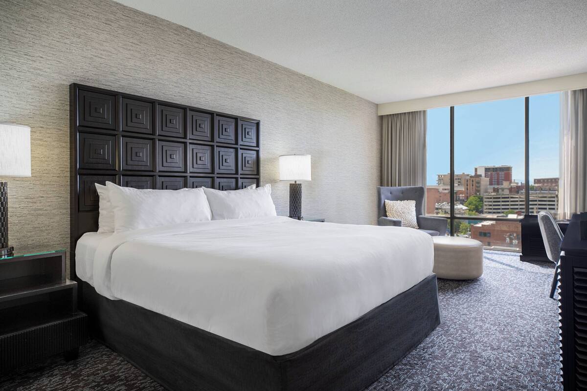 A hotel room with a large bed, a desk, a chair, and a view of the city.
