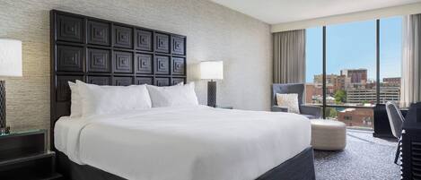A hotel room with a large bed, a desk, a chair, and a view of the city.