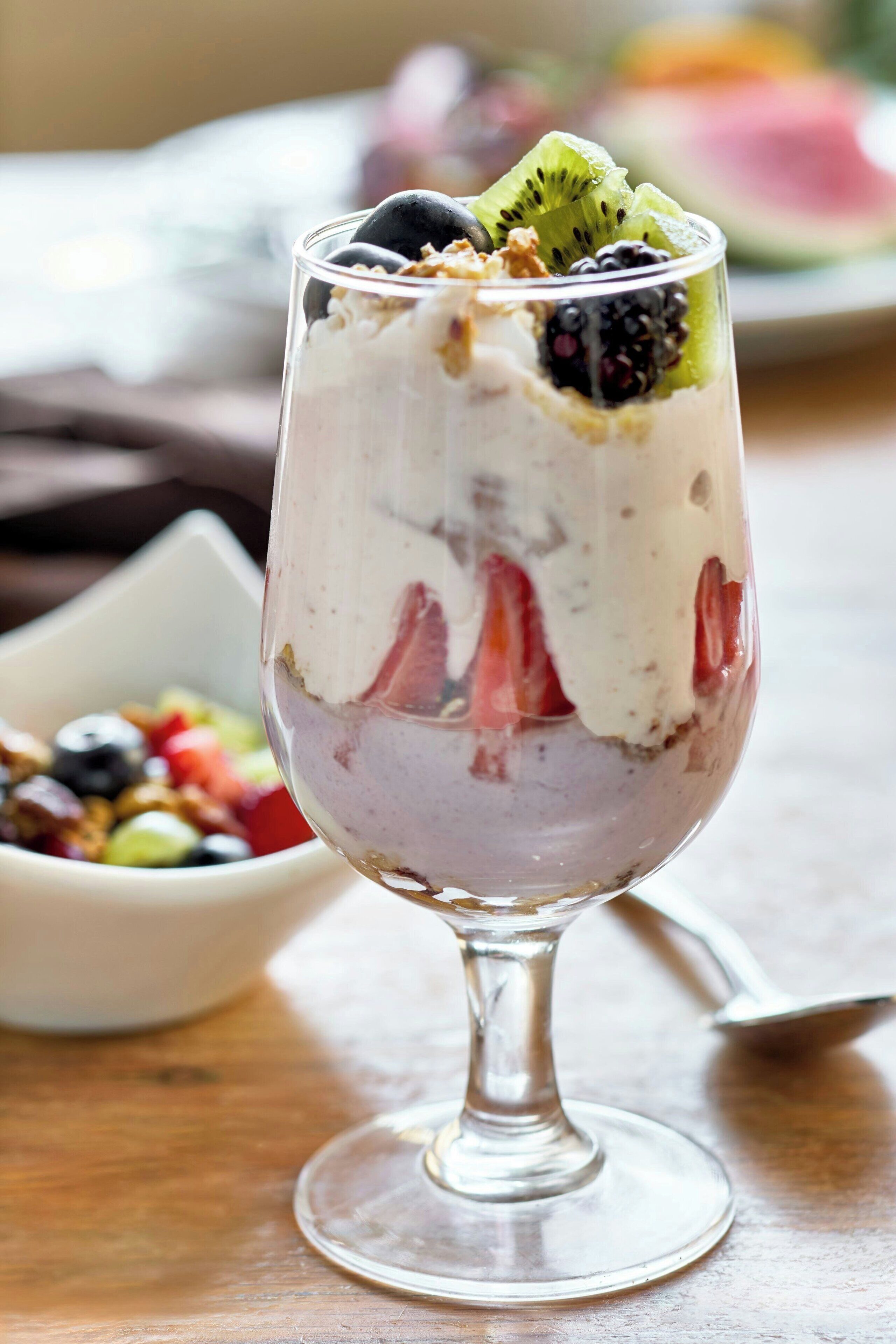 A dessert in a glass with layers of cream, fruit, and granola.