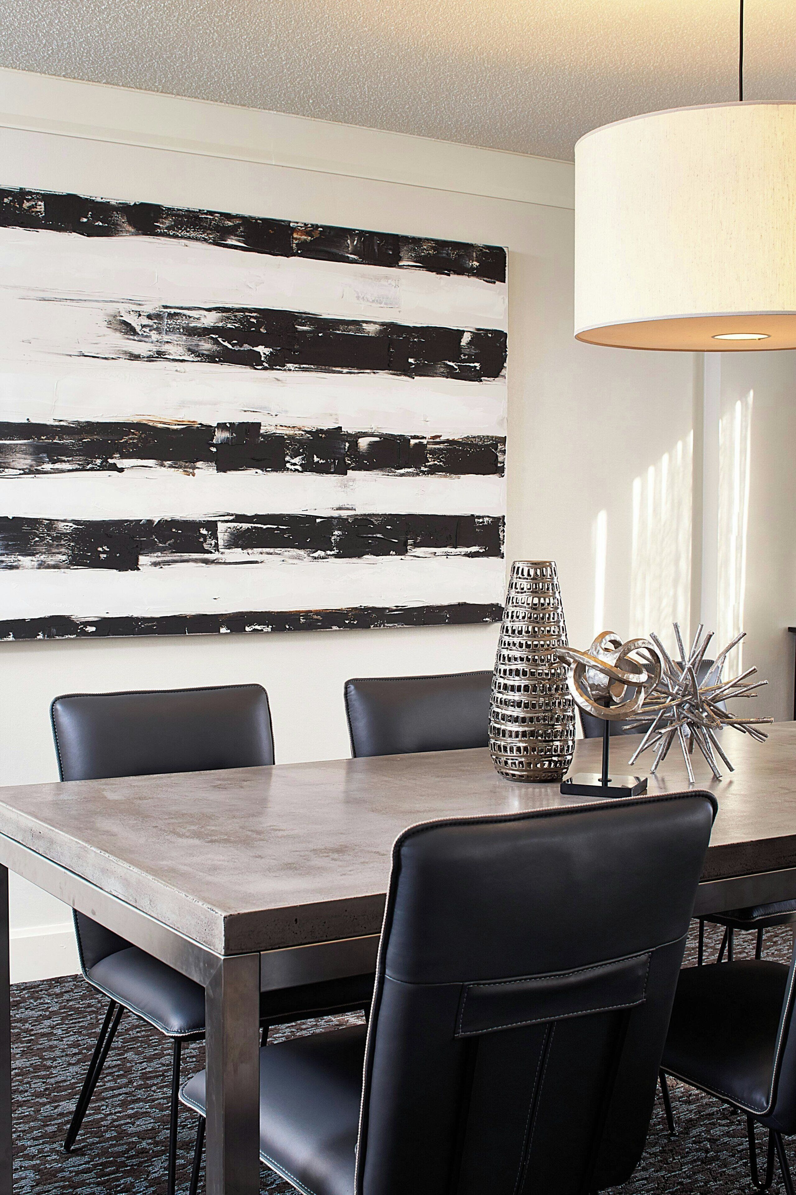 Un comedor con mesa de madera, sillas negras, un cuadro abstracto moderno y una escultura metálica decorativa.