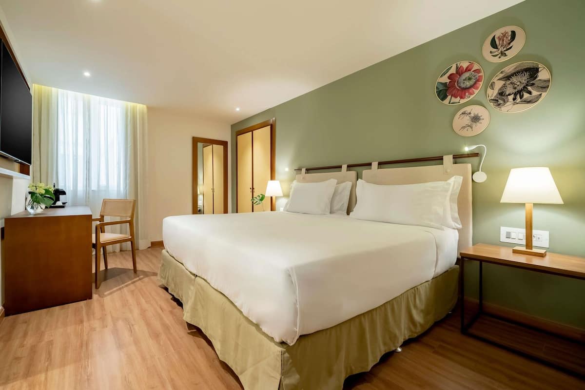 A hotel room with a bed, bedside table, desk, chair, and wall decorations.